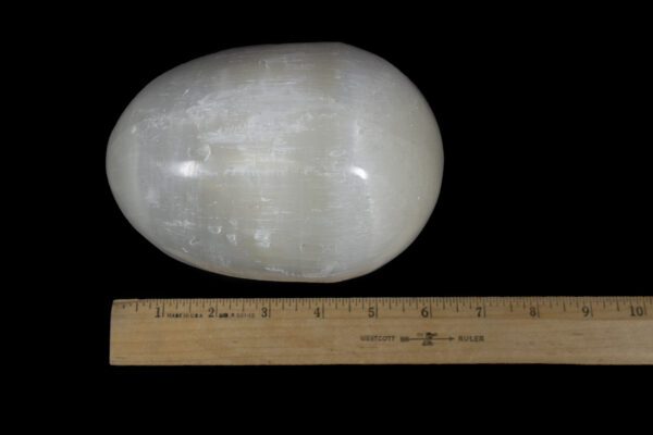 Large egg-shaped selenite stone next to ruler for comparison