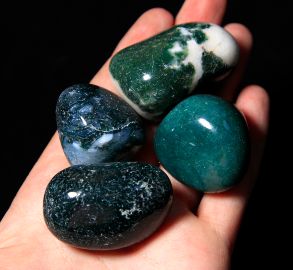 Pile of Medium Tumbled Moss Agate in hand for size comparison