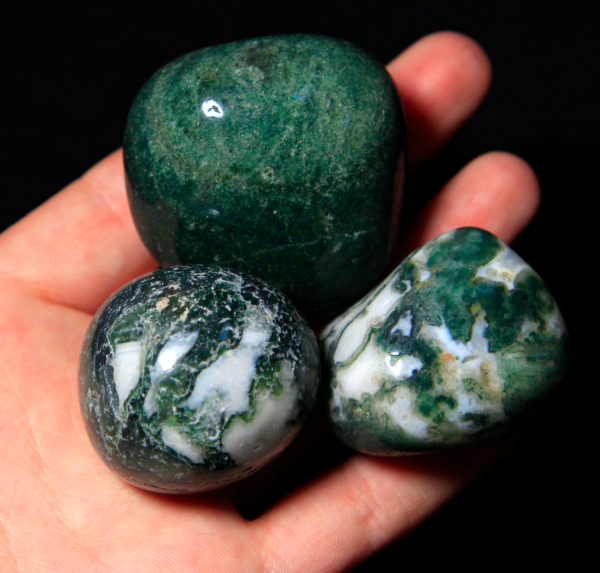 Pile of Large Tumbled Moss Agate in hand for size comparison