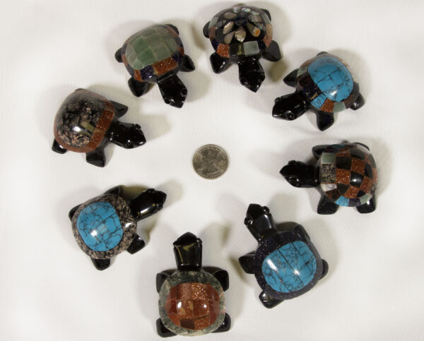 Eight small black decorative turtles centered around a quarter for size comparison