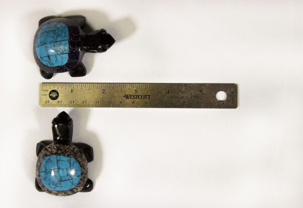 Two small black decorative turtles with blue shells next to a ruler