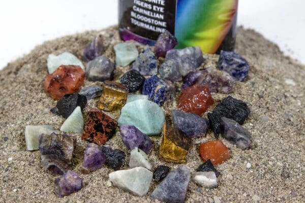 Rainbow Bag with pieces of Amethyst, Sodalite, Kyanite, Tigers Eye, Amazonite, Carnelian, Bloodstone, Tourmaline stones placed in sand